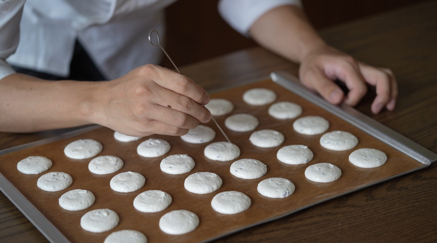 專業甜點師正用工具細緻調整馬卡龍餅殼，展現這款如香水般結構精密的法式甜點製作過程。